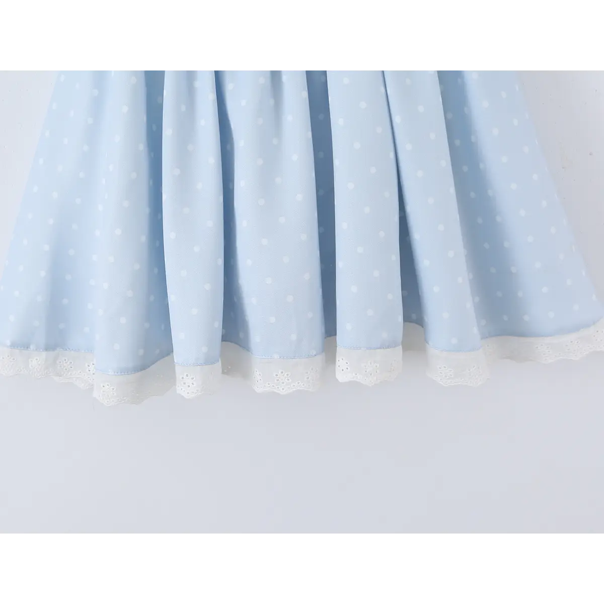  Close-up of the lace-trimmed hem on the flared skirt of a light blue polka dot dress.