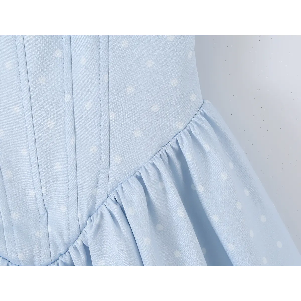 Close-up of the corset-style waist seam on a light blue polka dot dress, showing the bodice-to-skirt transition.