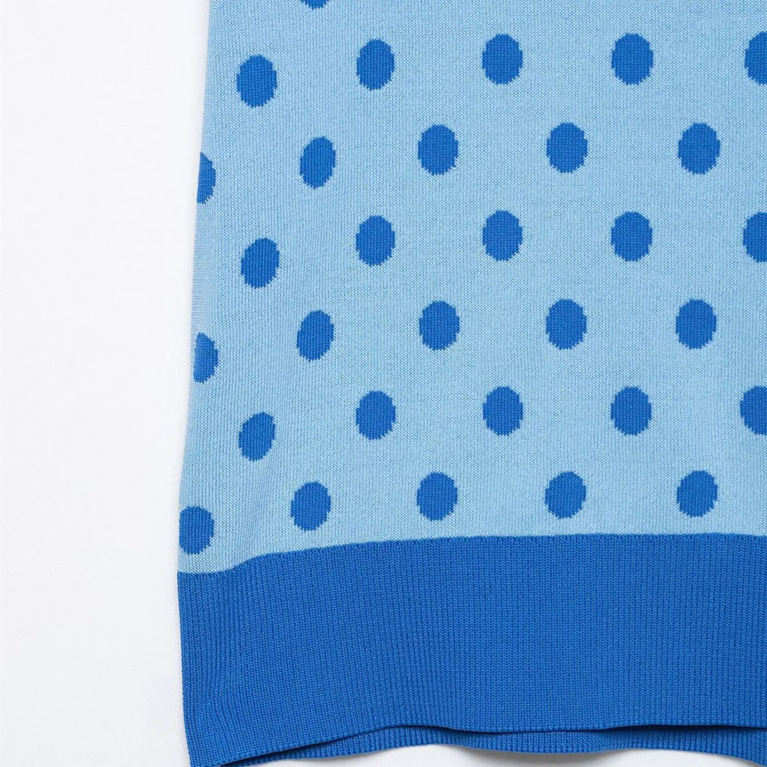 Close-up of the ribbed hem on the light blue polka dot knit polo top, showing the color-block trim