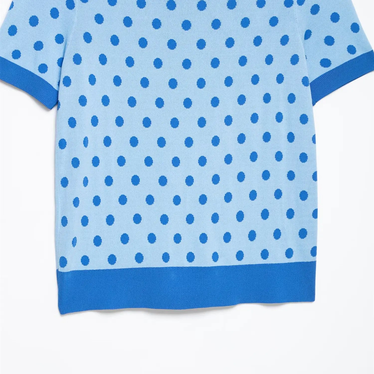 Close-up of the side hem and polka dot pattern on the light blue knit polo top