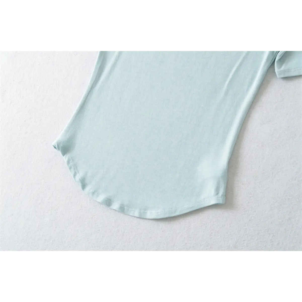 Close-up of light blue ribbed half-turtleneck top's curved hem, showing stitching