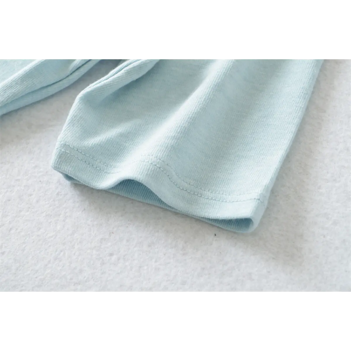 Close-up of the double-stitched cuff on the light blue ribbed half-turtleneck top