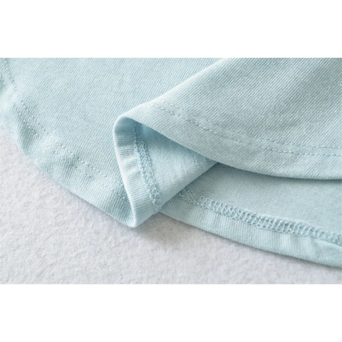 Partial view of the curved hem on the light blue ribbed half-turtleneck top