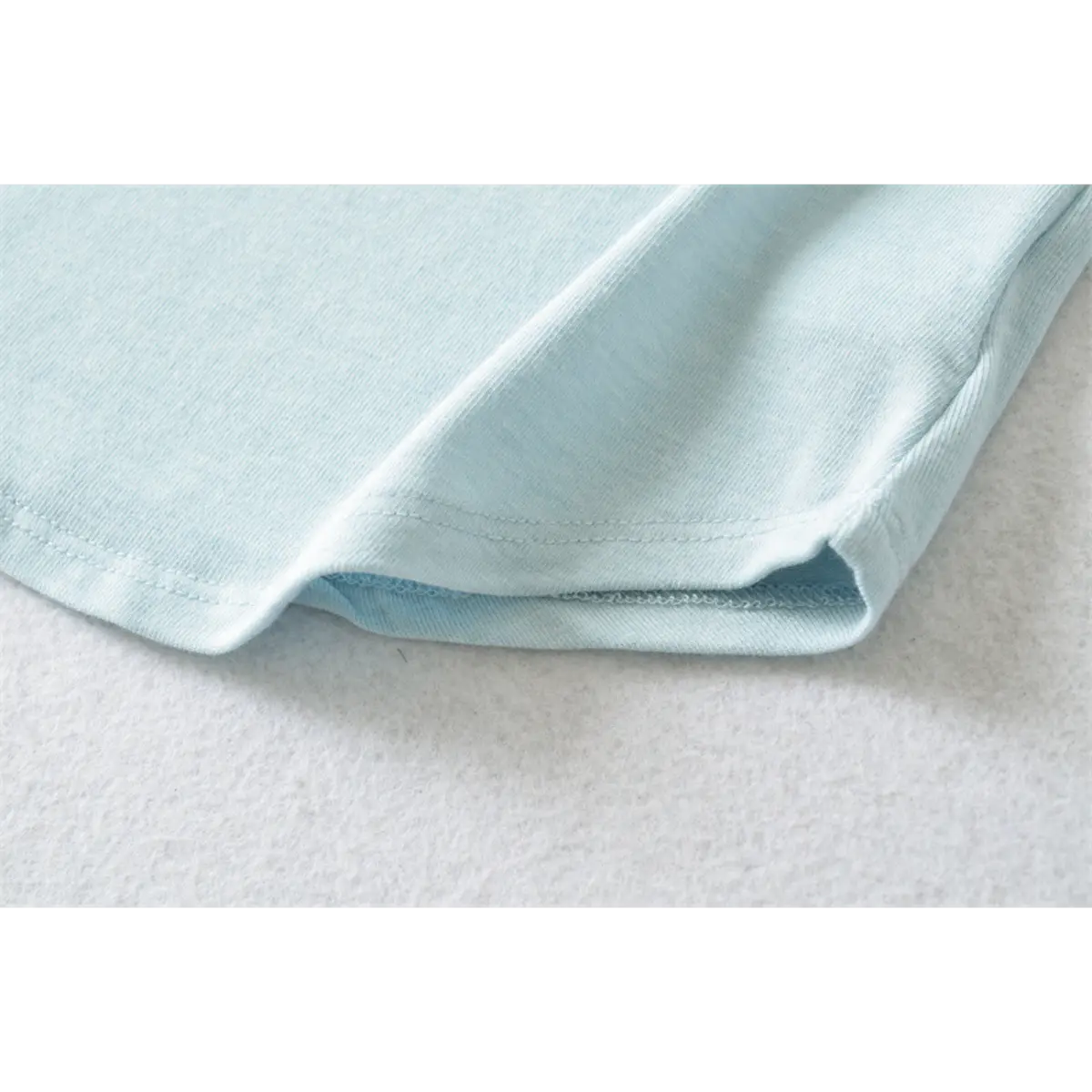 Close-up of the curved hem stitching on the light blue ribbed half-turtleneck top