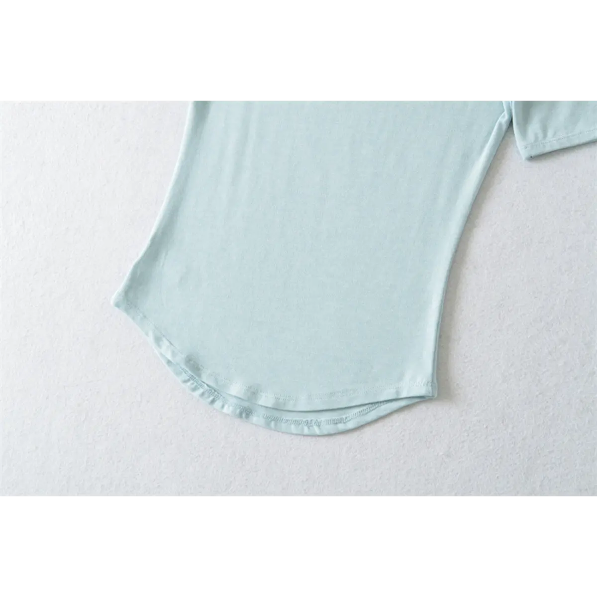 Partial view of the curved hem on the light blue ribbed half-turtleneck top
