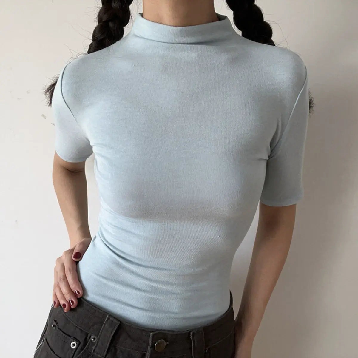 Lifestyle shot of form-fitting light blue ribbed half-turtleneck short-sleeve top, tucked into jeans