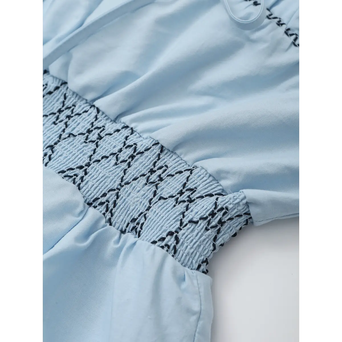 Close-up of the black geometric stitch pattern on the smocked waistband of the light blue top