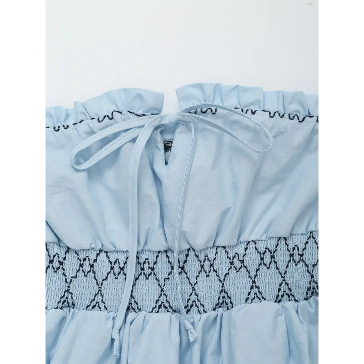Close-up of the front tie detail and back zipper on the light blue smocked strapless top