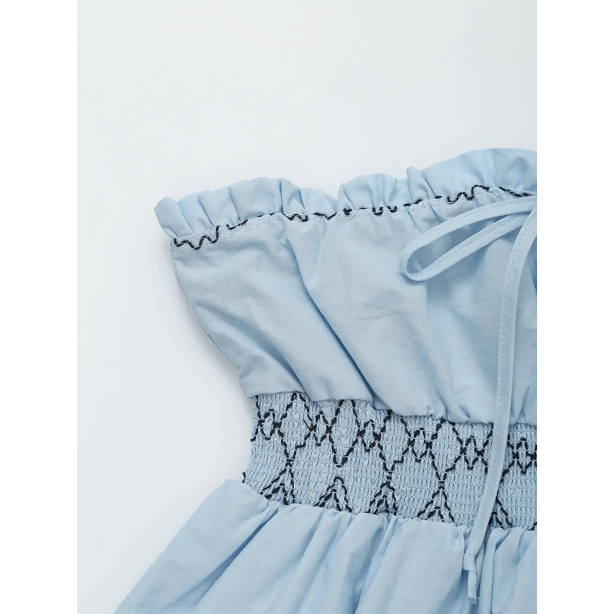 Close-up of the elastic smocked waist and lace trim on the light blue strapless top