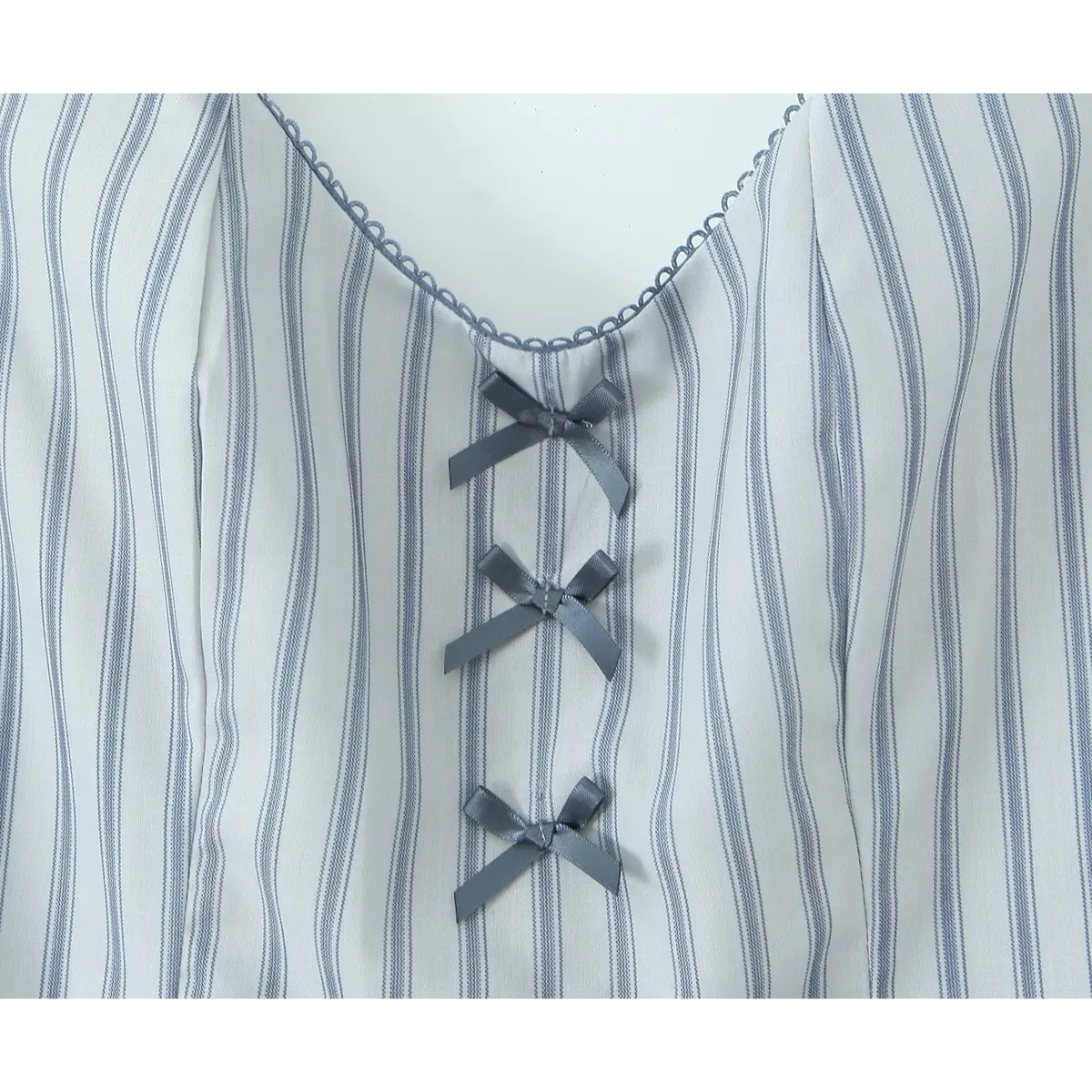 Close-up of the gray ribbon bows on the front bodice of the light blue striped halter dress, set against the striped pattern and scalloped neckline.