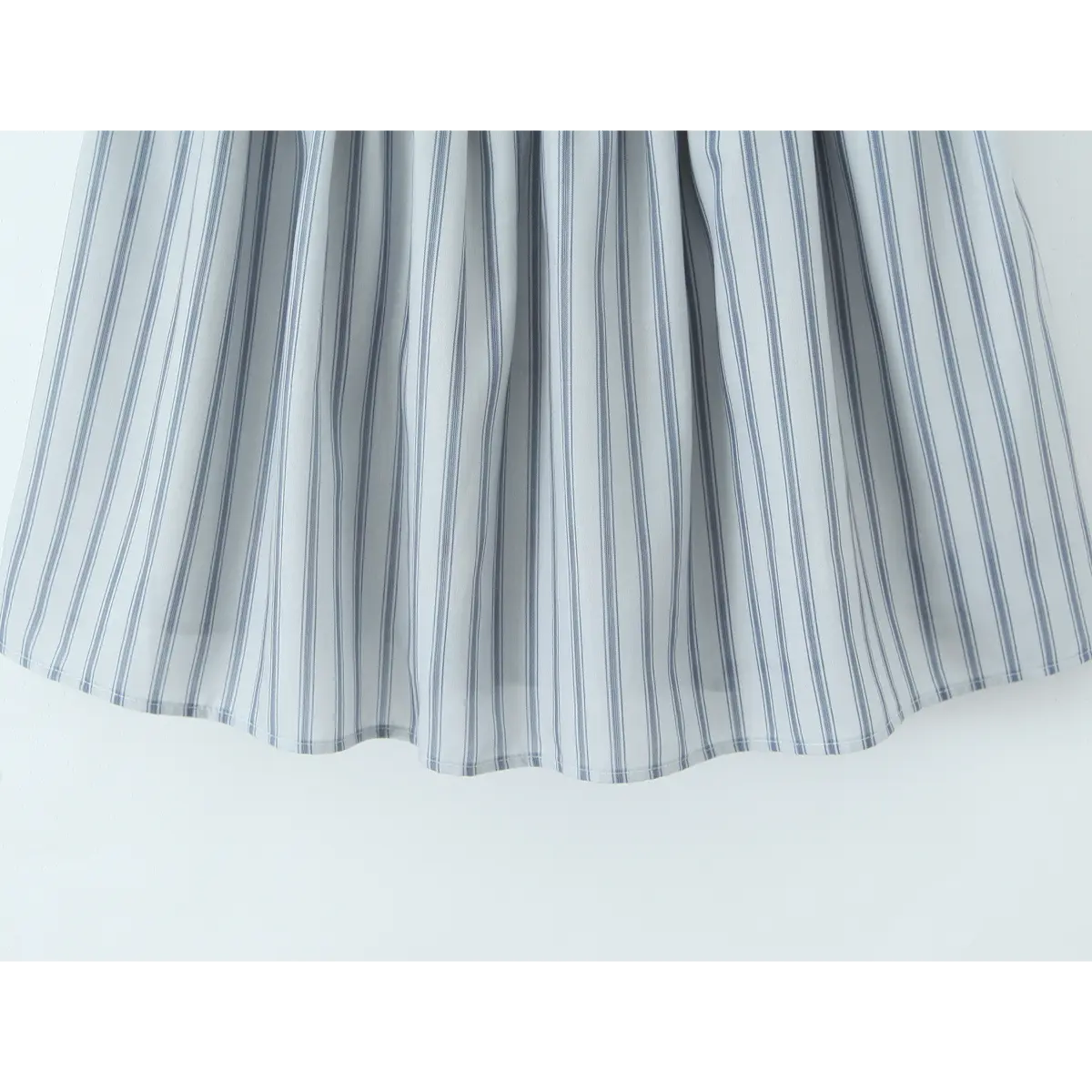 Close-up of the flared skirt hem on the light blue striped halter dress, showing the fabric drape and pattern.