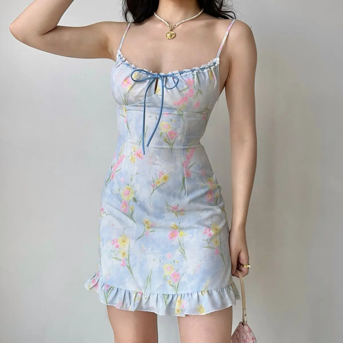  Full view of a light blue watercolor floral mini dress, displaying the spaghetti straps, lace trim, blue bow, and ruffled hem.