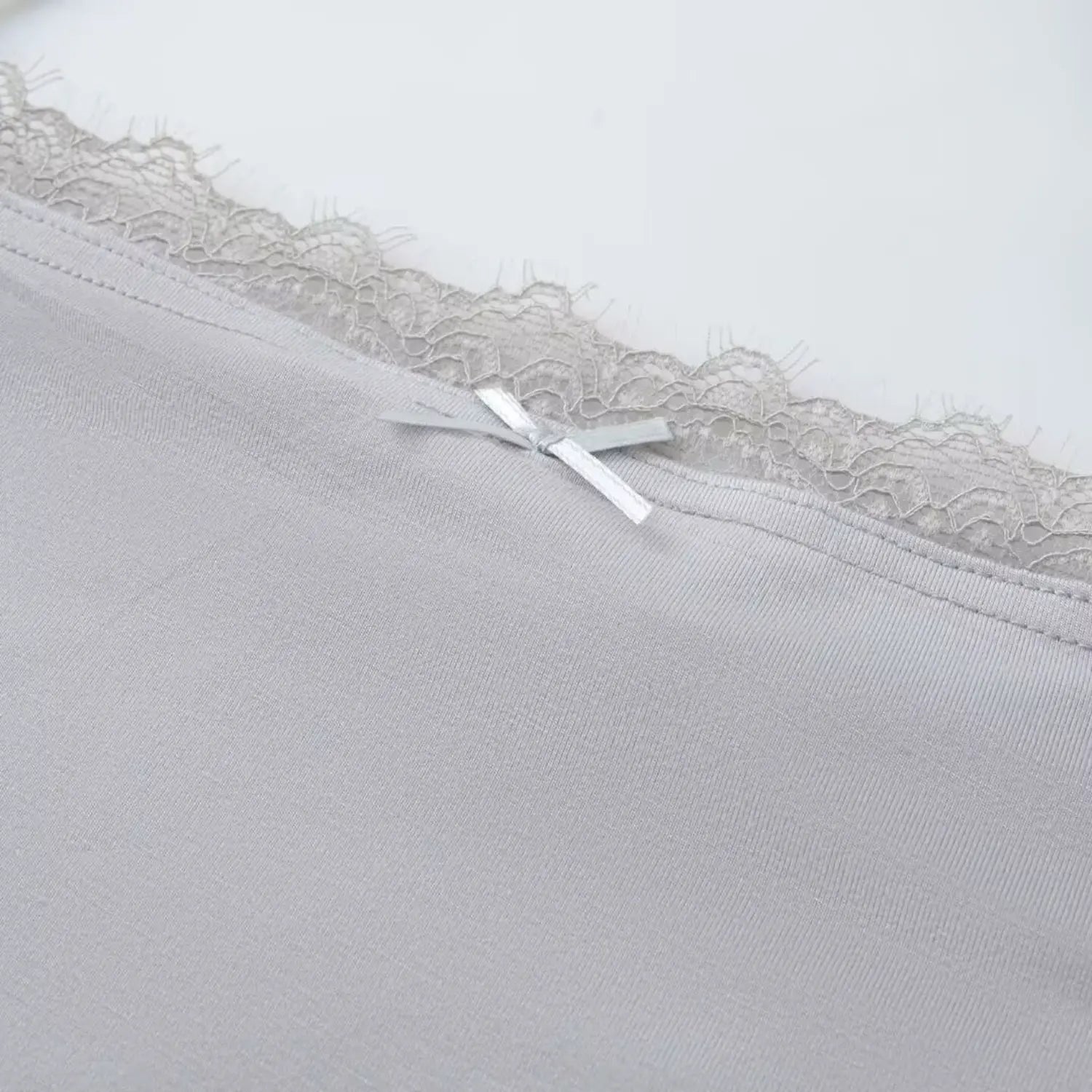 Macro close‑up of lace scalloped trim and small front bow on light gray halter cami