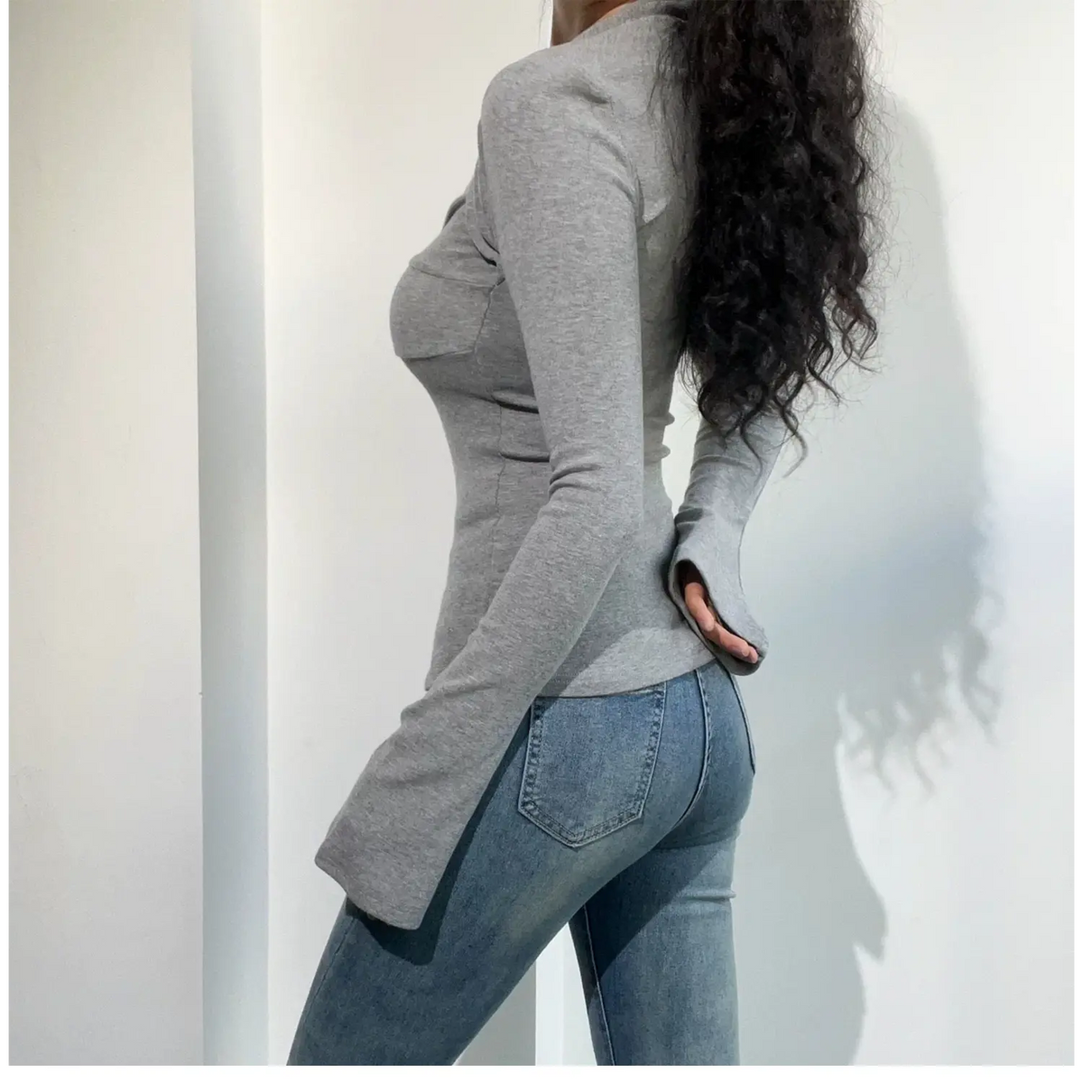 Side back view of model in light gray twist front long sleeve top, slim fitted silhouette and flare long sleeves