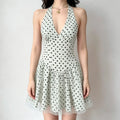 Model wearing a light green halter-neck mini dress with black polka dots, a deep V-neck, and a flared skirt with a sheer tulle underlayer.