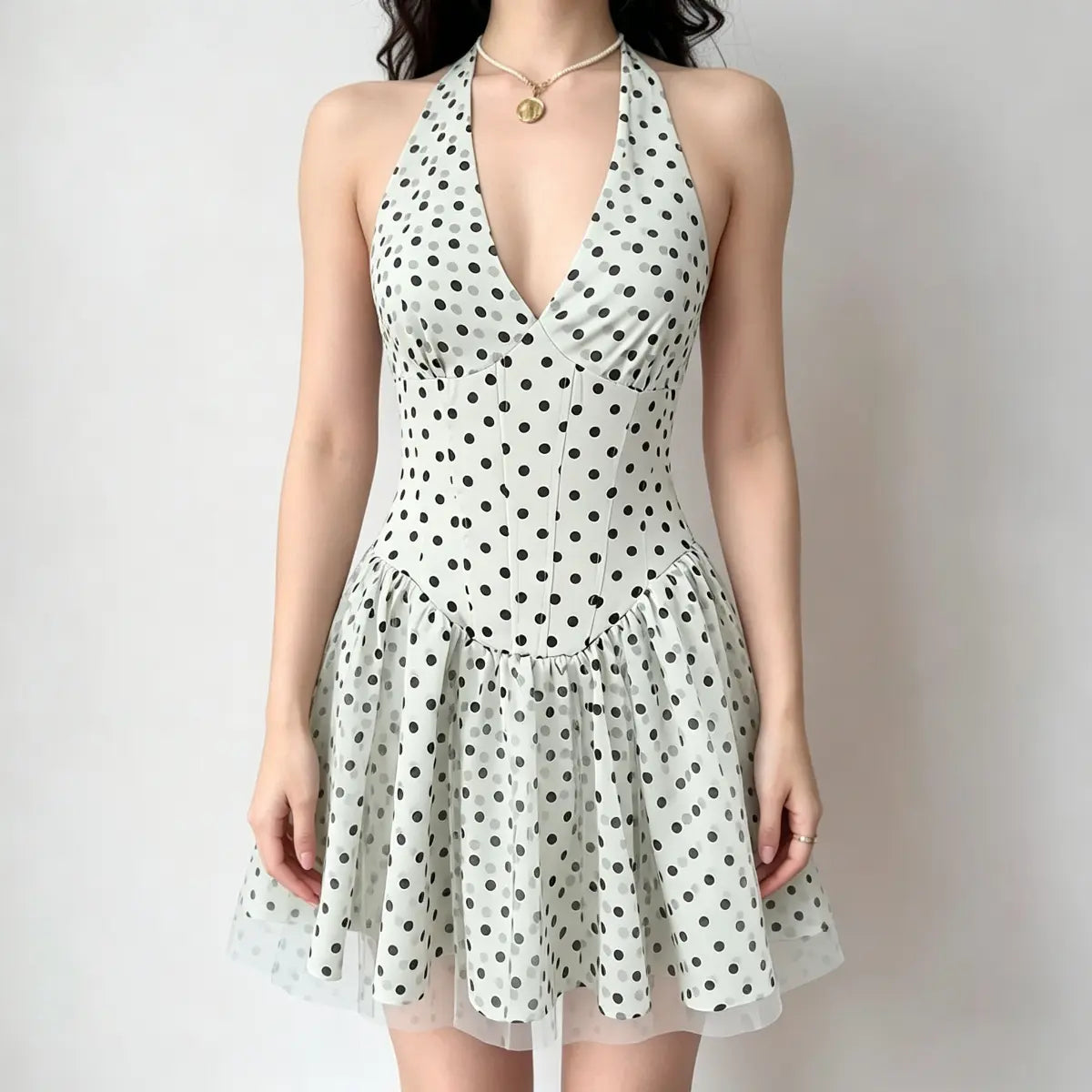 Model wearing a light green halter-neck mini dress with black polka dots, a deep V-neck, and a flared skirt with a sheer tulle underlayer.