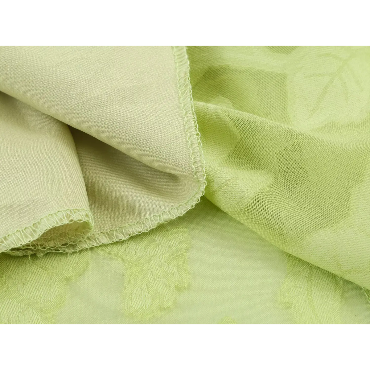 Light green jacquard fabric showing outer textured layer and smooth inner lining with overlock stitching