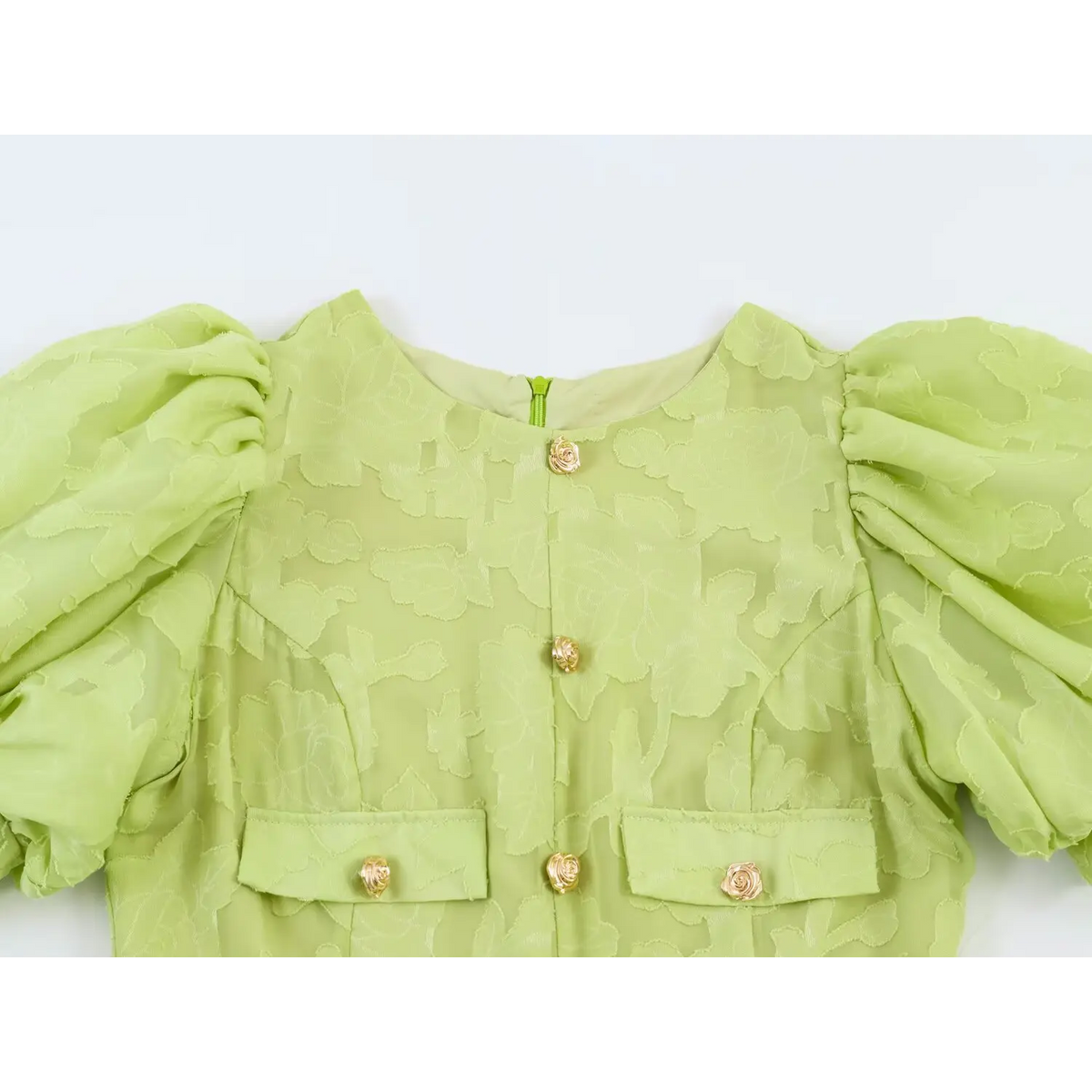 Close-up of dress bodice, light green floral jacquard fabric, gold rose shaped decorative buttons and fake pocket details