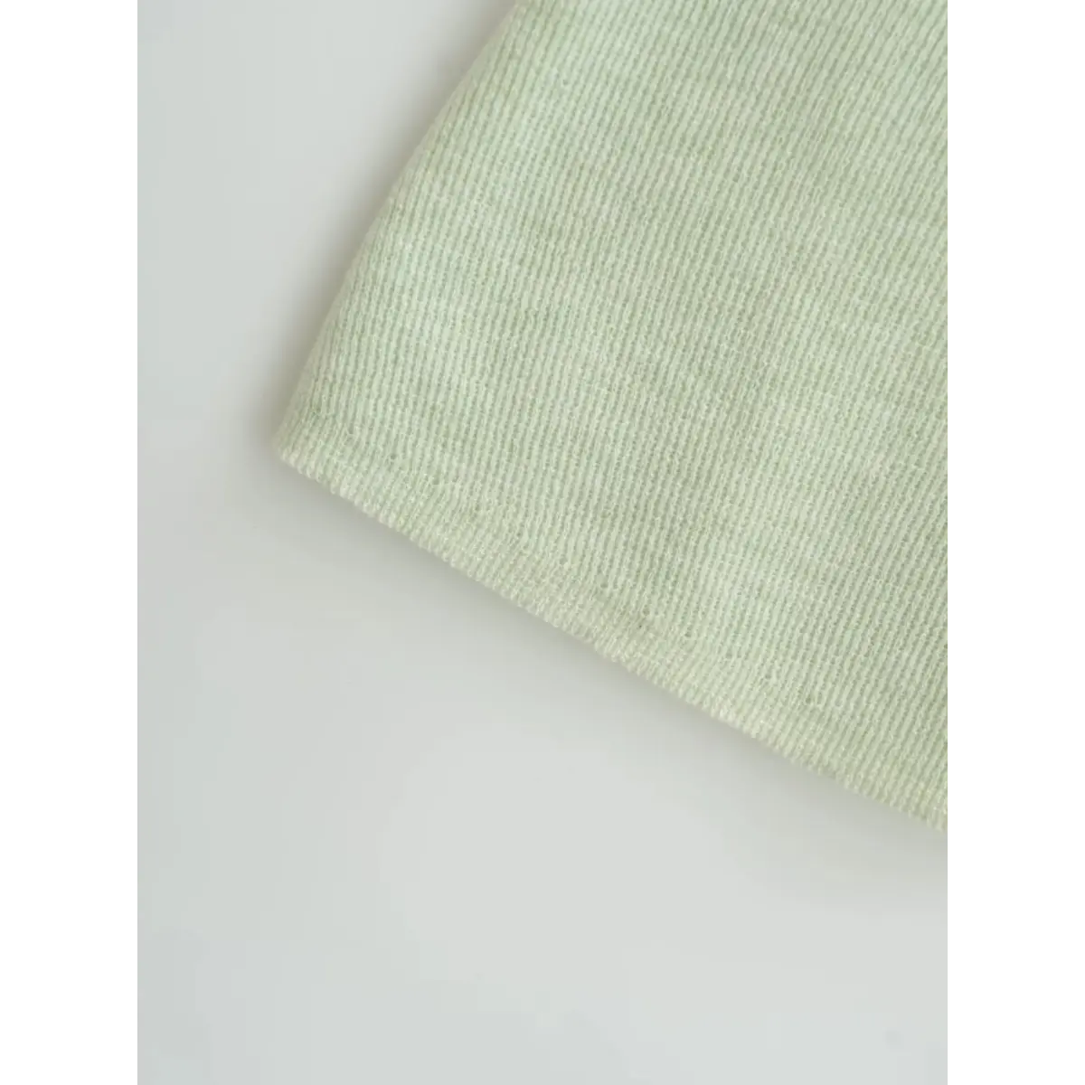Close-up view of the fabric and hem on a light green ribbed off-the-shoulder top, showing the fine knit texture and finished edge.