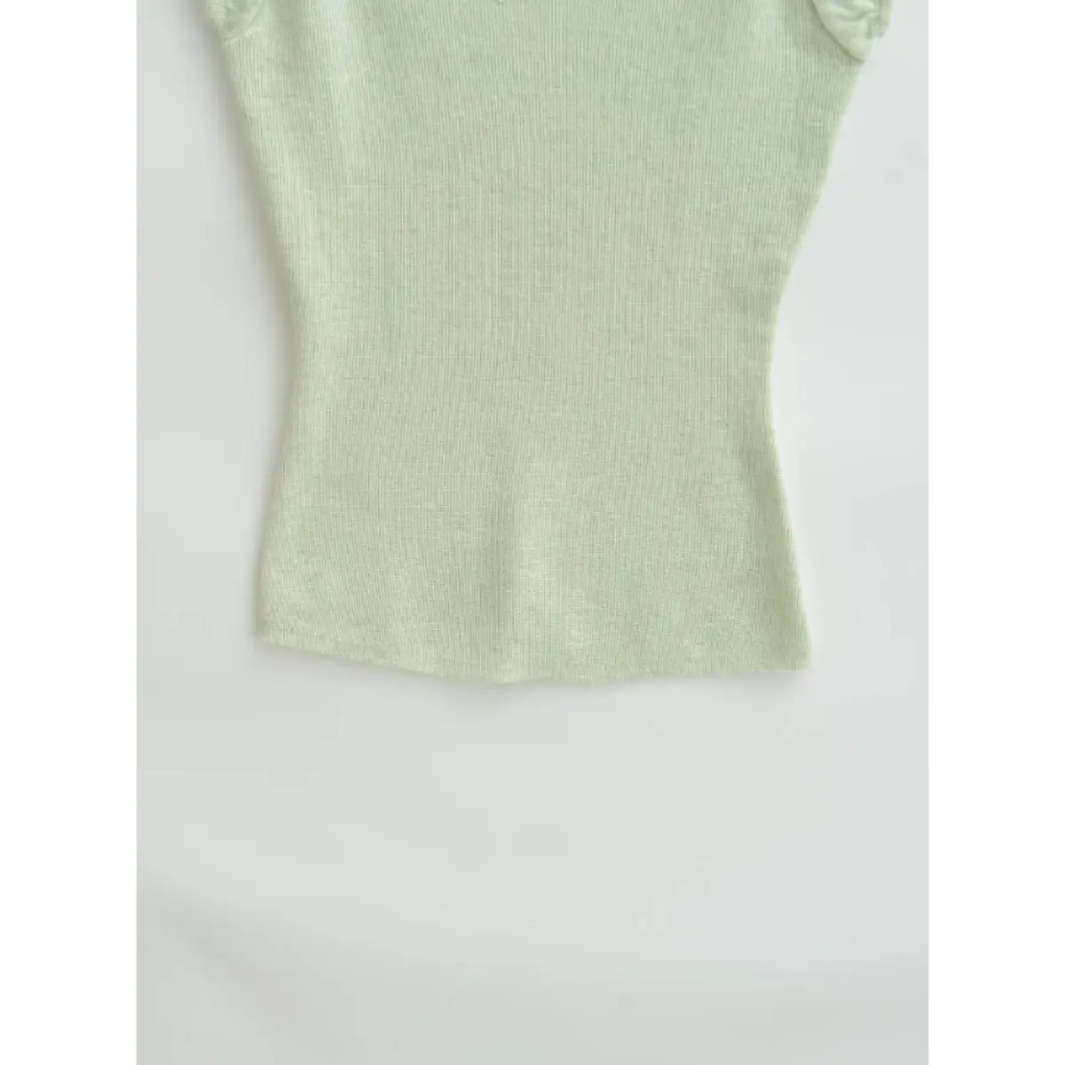 Close-up view of the hem on a light green ribbed off-the-shoulder top, showing the straight cut and fine ribbed texture.