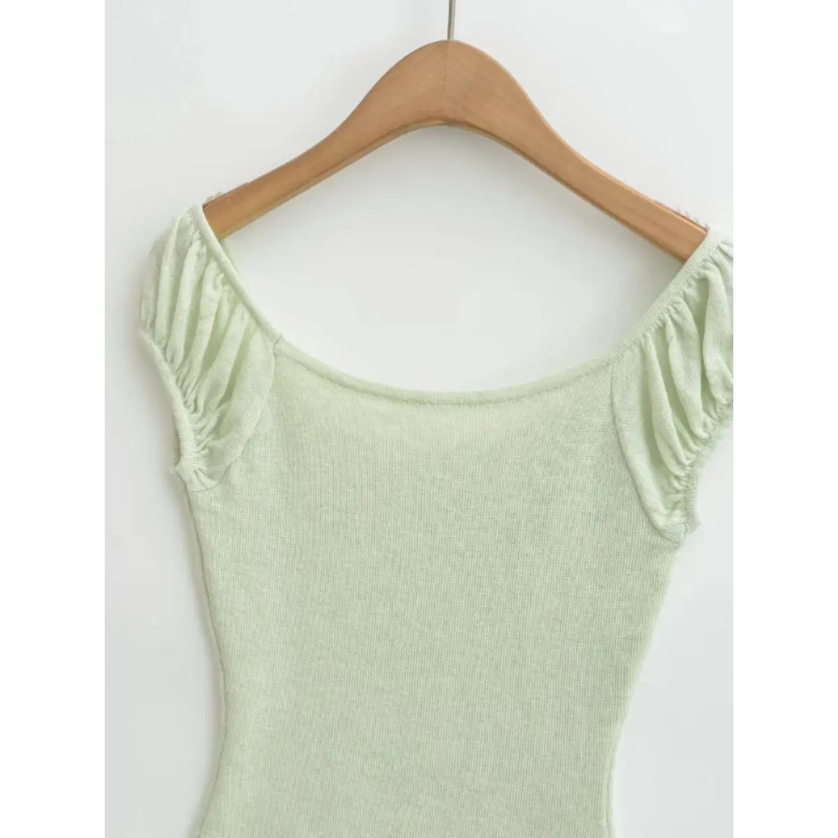 Back view of a light green ribbed off-the-shoulder top hanging on a wooden hanger, showing the wide scoop neckline and puff sleeves.