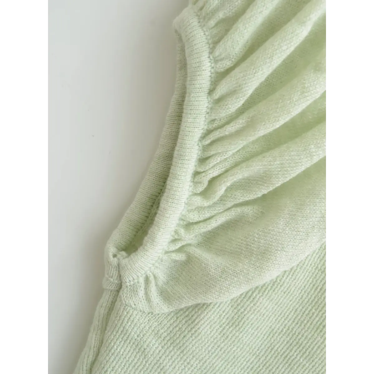 Close-up detail of the puff sleeve on a light green ribbed off-the-shoulder top, showing the gathered stitching and soft knit texture.