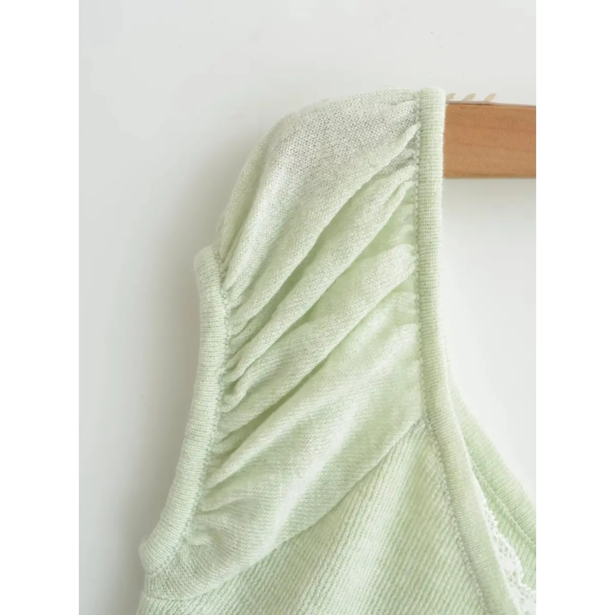 Close-up detail of the puff sleeve and seam on a light green ribbed off-the-shoulder top, showing the gathered construction and knit texture.
