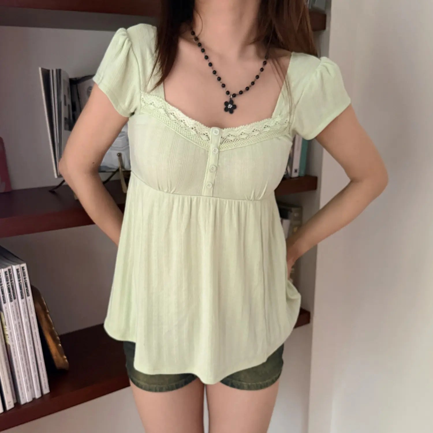 Lifestyle shot of a woman in a light green square-neck puff sleeve top, standing in front of a bookshelf
