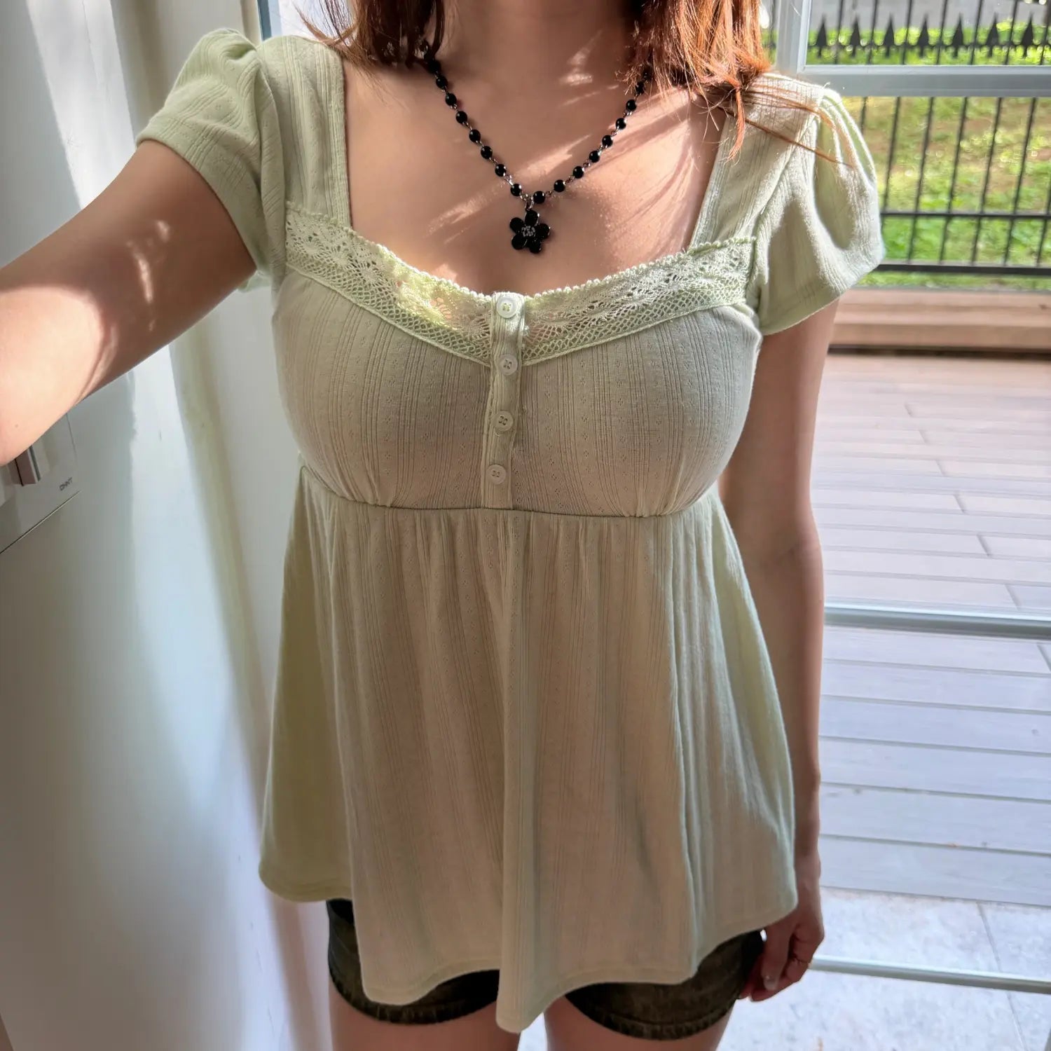 Close-up shot of a woman in a light green square-neck puff sleeve top, showing the lace trim and button placket in sunlight