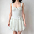 Model wearing a light green corset-style dress with a lace-trimmed bustier, gathered tulle skirt, and wide straps.