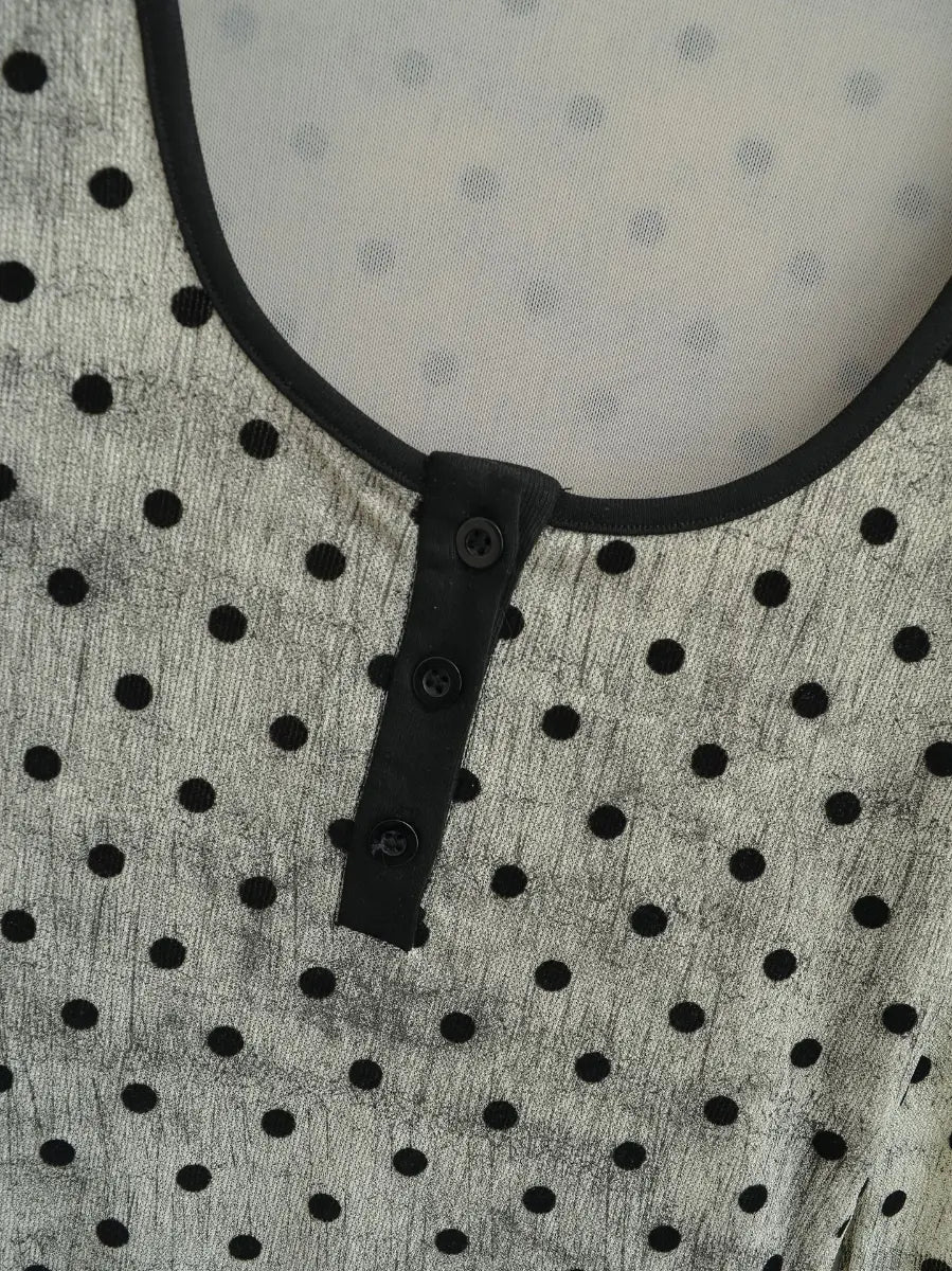 Close-up of the black henley button placket and contrast neckline trim on the light grey polka dot top