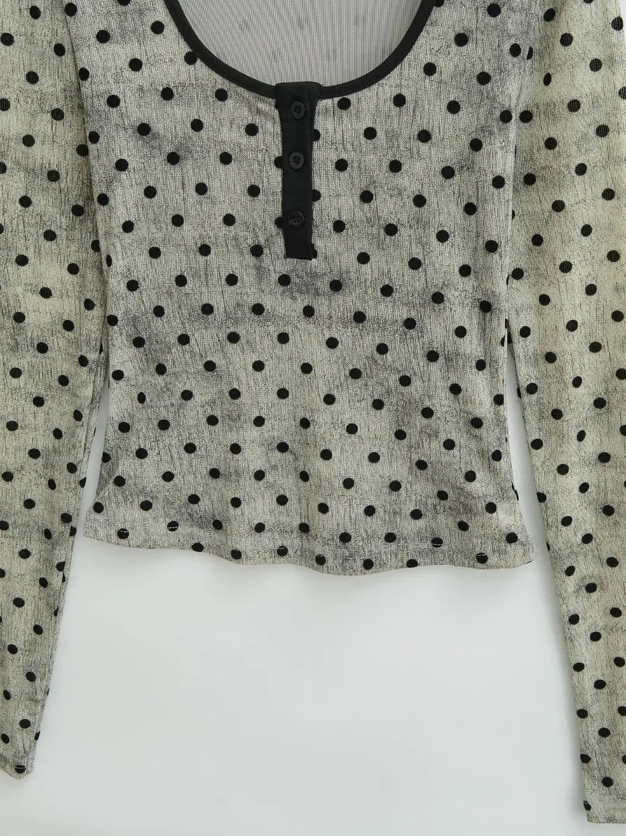 Close-up of the fitted silhouette and finished hem on the light grey polka dot long-sleeve top