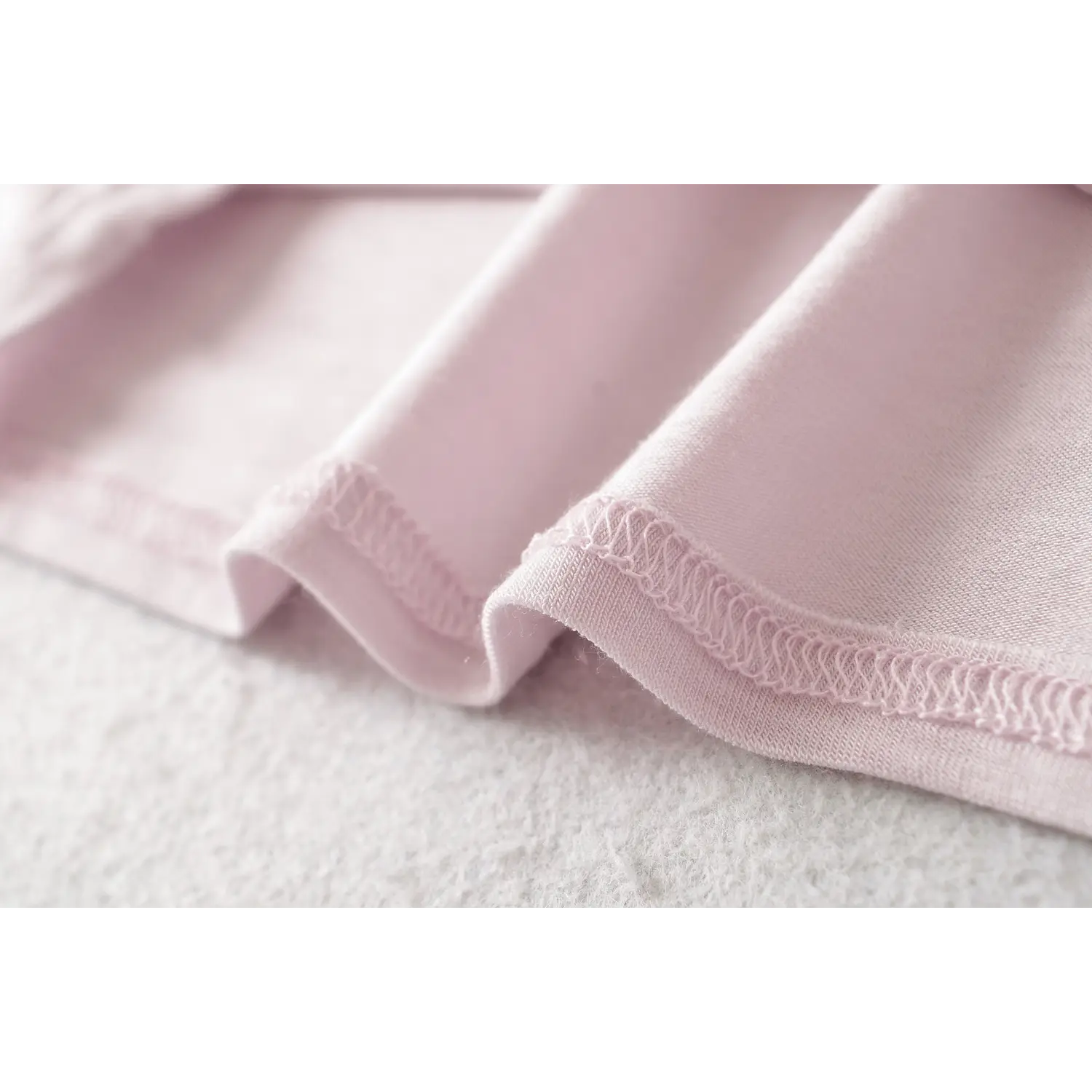 Light lilac fake two long sleeve top hem flat close-up, wavy elastic overlock waist cinched curved hem fine knit binding craft white background shot