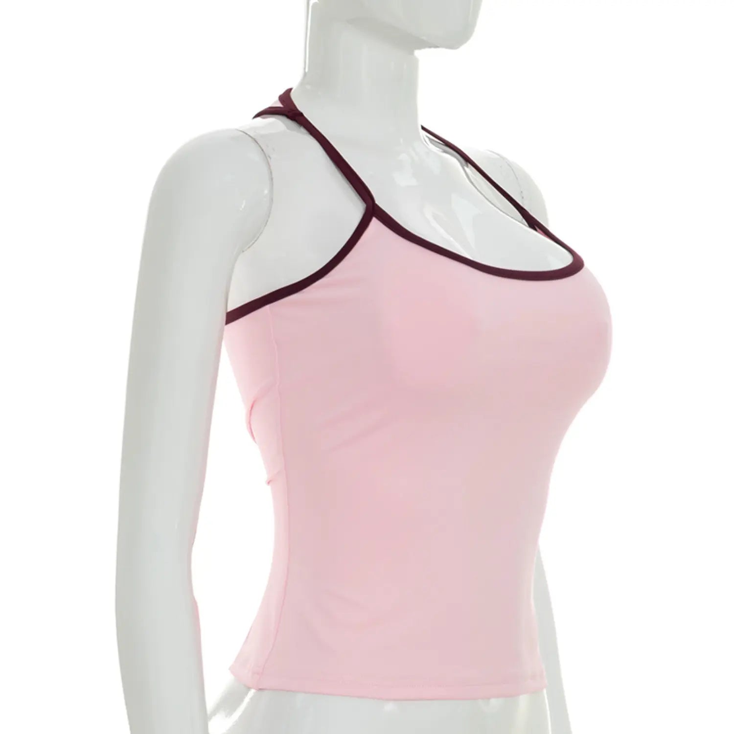 Side profile white studio mannequin shot of fitted halter crop tank top, solid pastel pink fabric with burgundy contrast neck piping, slim shaping waist, thin halter straps creating open racerback cutout