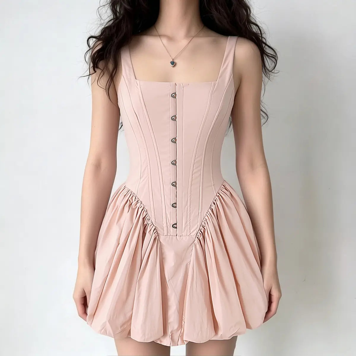 Full-body shot of a woman wearing a light pink corset-style dress with a bubble hem and eyelet details.