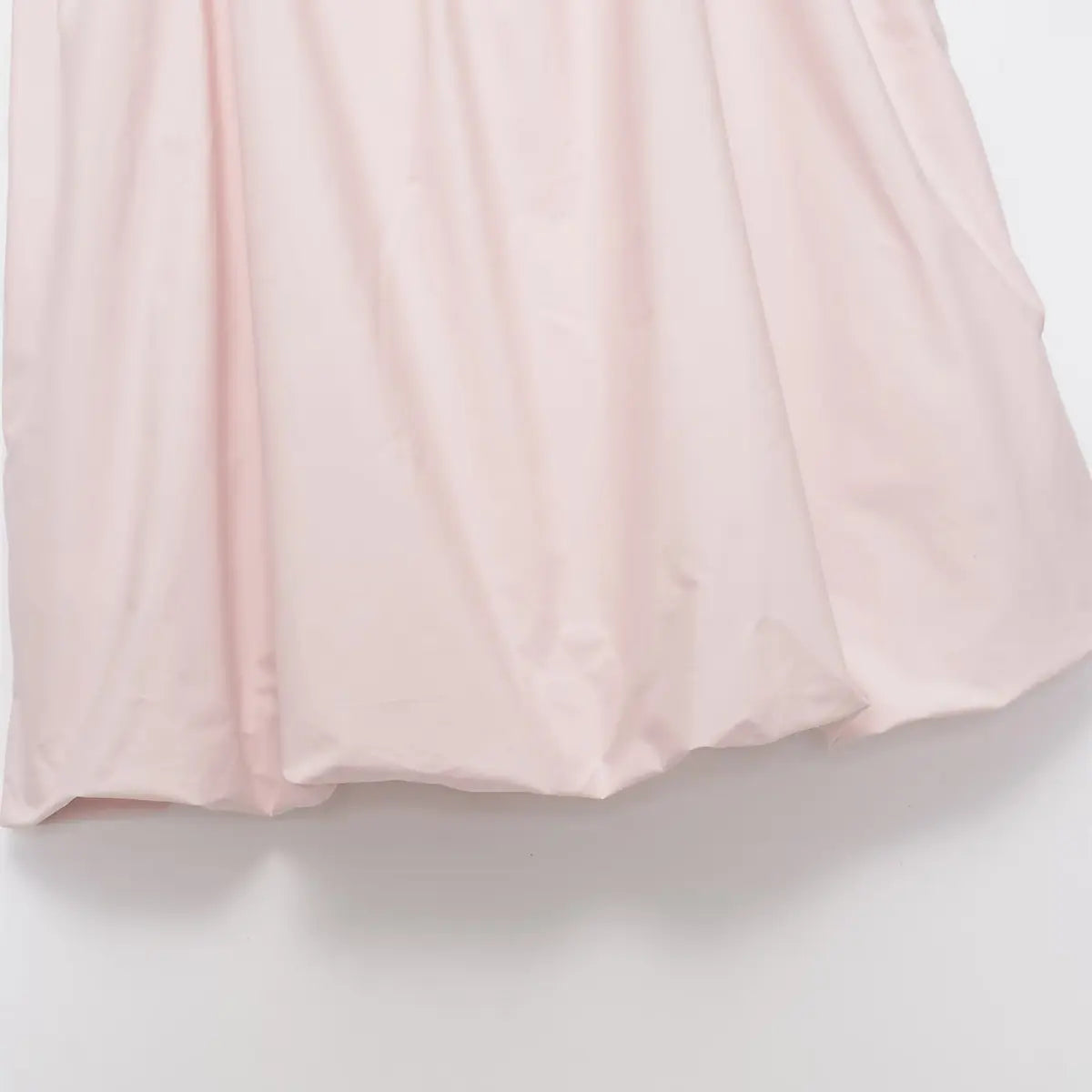 Hem view of the light pink cotton dress, showing the voluminous, bubble-style finish and soft fabric drape
