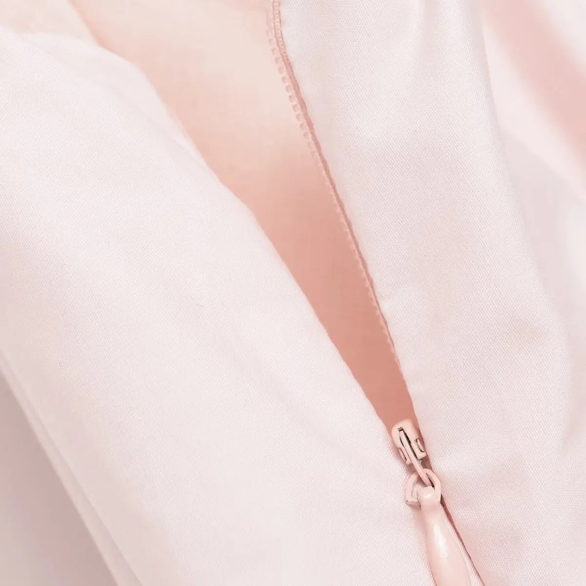 Close-up of the side zipper on the light pink cotton dress, showing the matching pink pull and neatly stitched seam