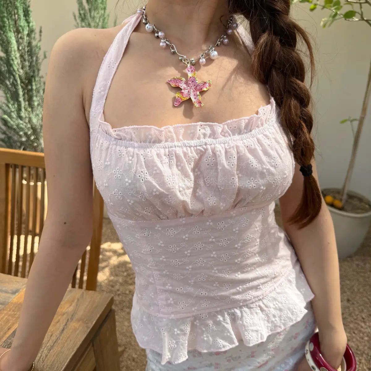 Close-up of a light pink eyelet halter top, showing the corset-style bodice, ruffled neckline, and peplum hem.