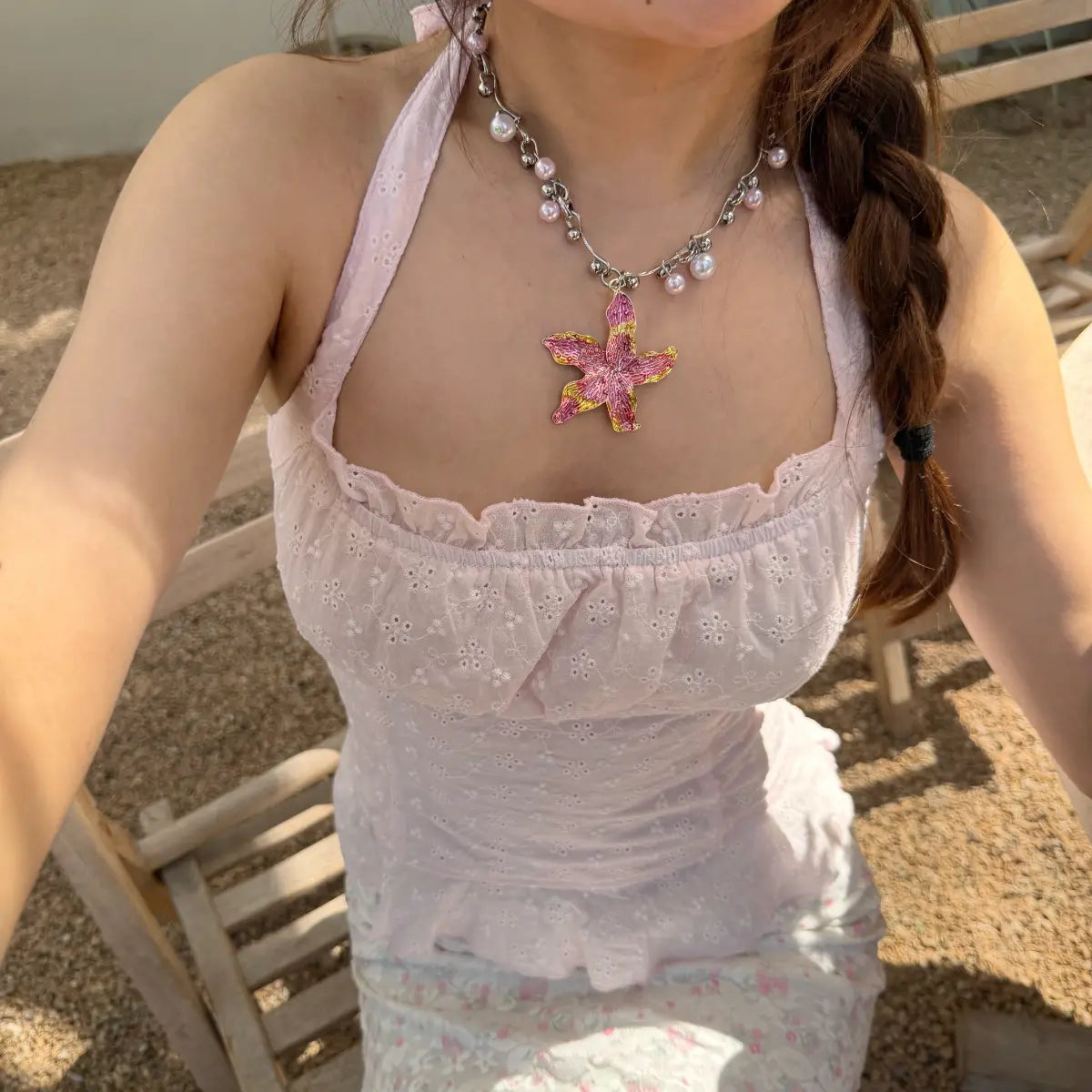  Sunlit view of a woman in a light pink eyelet halter top, accessorized with a starfish necklace and braided hair.

