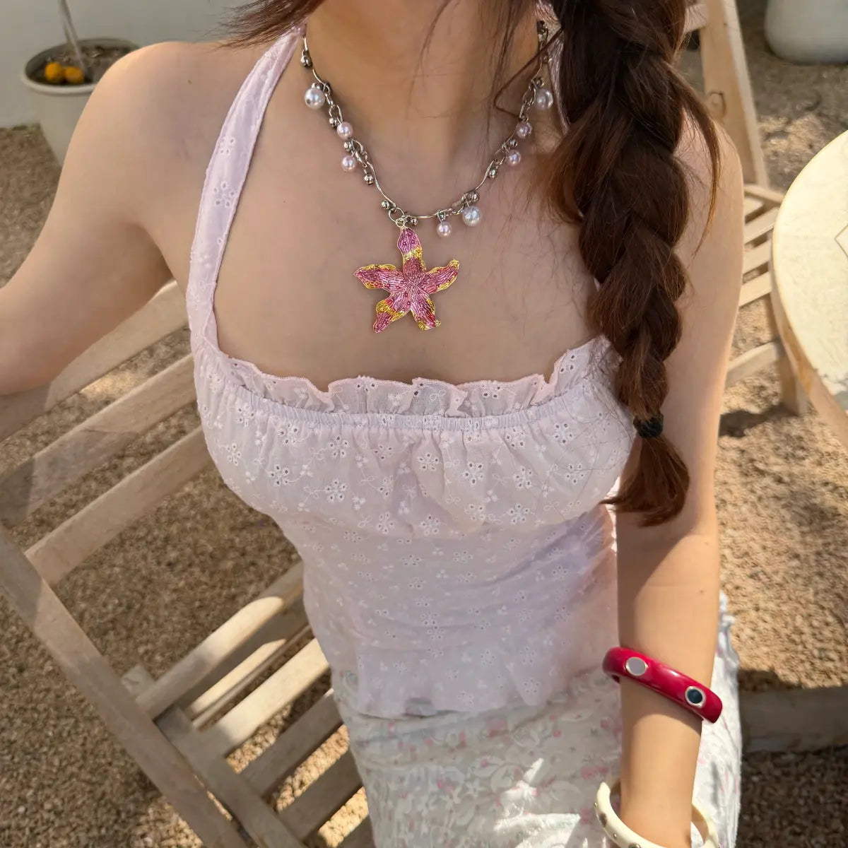 Close-up view of a woman in a light pink eyelet halter top, featuring a starfish pendant necklace and ruffled neckline trim.