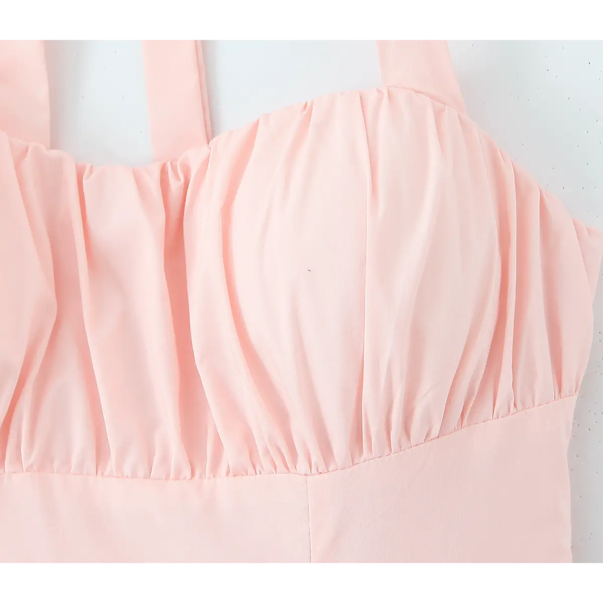 Close-up of the gathered bodice detail on a light pink halter maxi dress, showing the ruched front neckline.