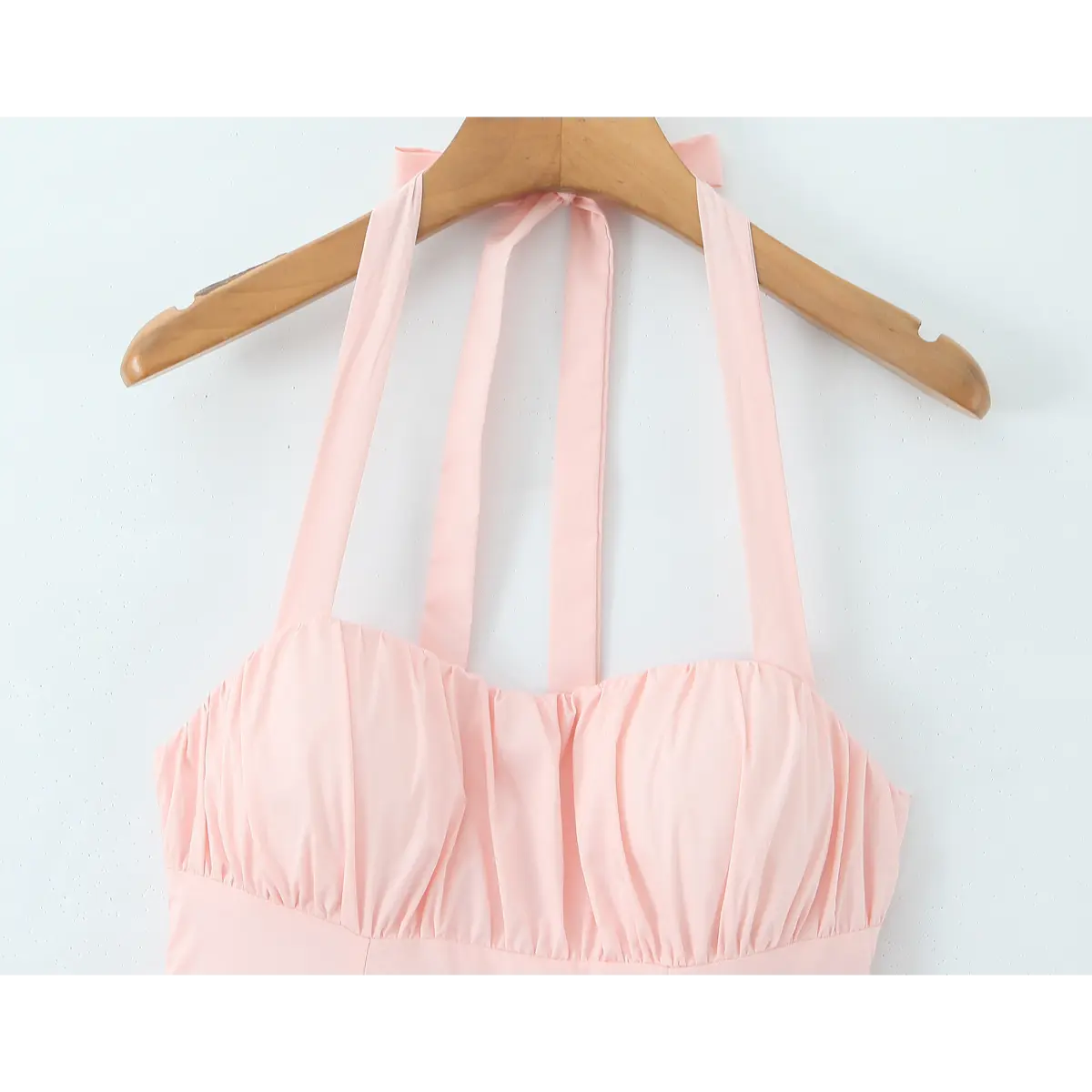 Front view of a light pink halter maxi dress on a wooden hanger, highlighting the halter straps and gathered bodice.

