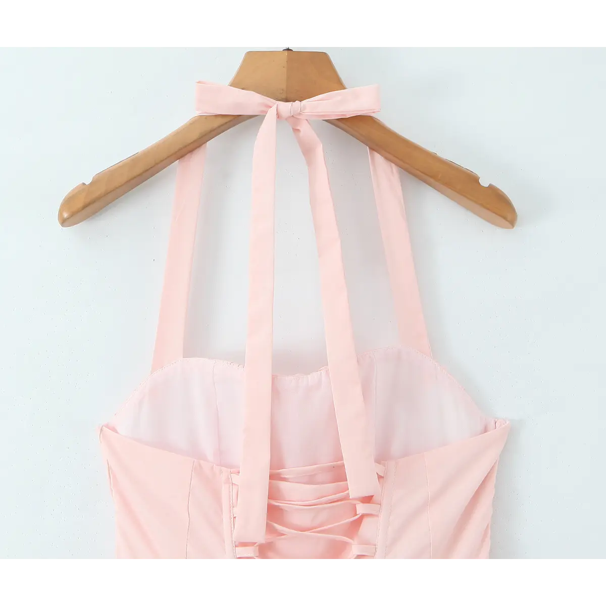  Light pink halter maxi dress hanging on a wooden hanger, showcasing the halter bow tie and corset-style back.