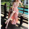 Full view of a woman in a light pink halter maxi dress by a pool, displaying the halter straps, corset waist, and flowing skirt.