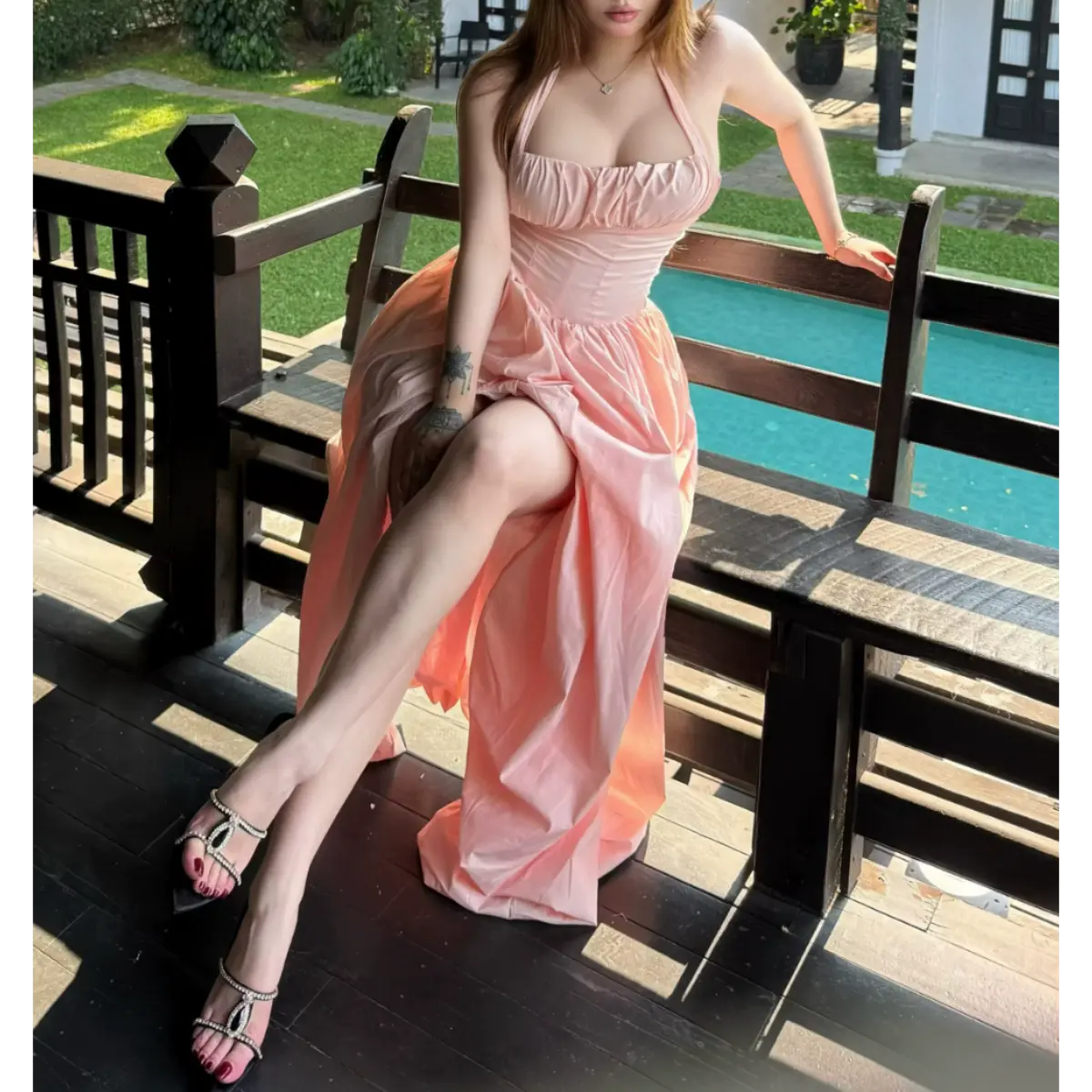 Full view of a woman in a light pink halter maxi dress by a pool, displaying the halter straps, corset waist, and flowing skirt.