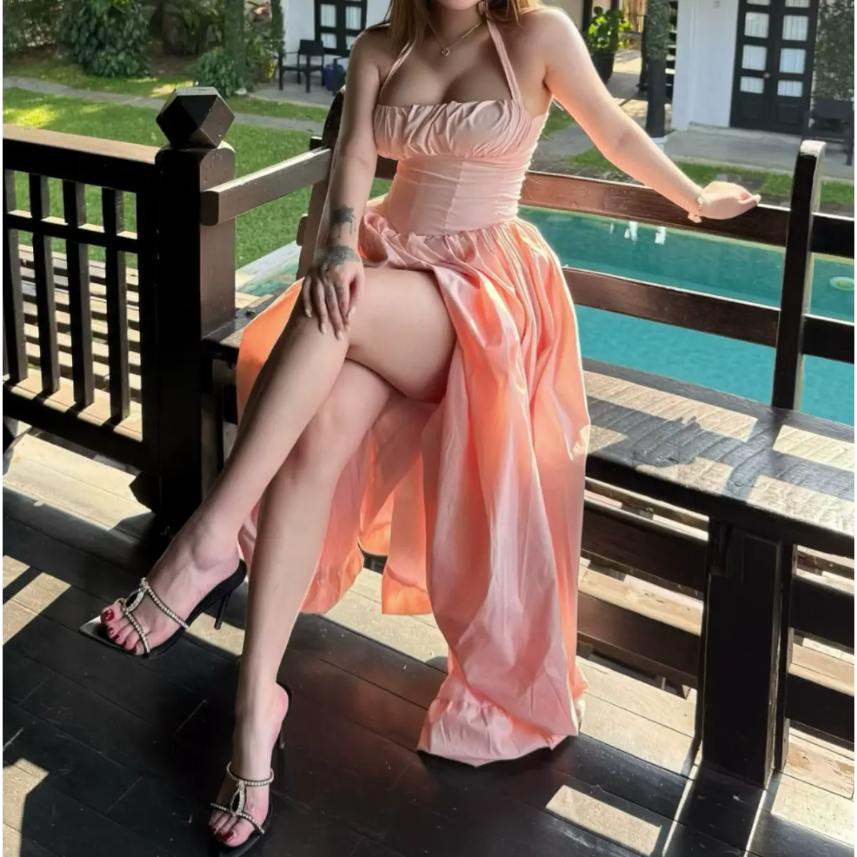 Woman in a light pink halter maxi dress sitting by a pool, showing the corset waist, gathered bodice, and voluminous skirt.