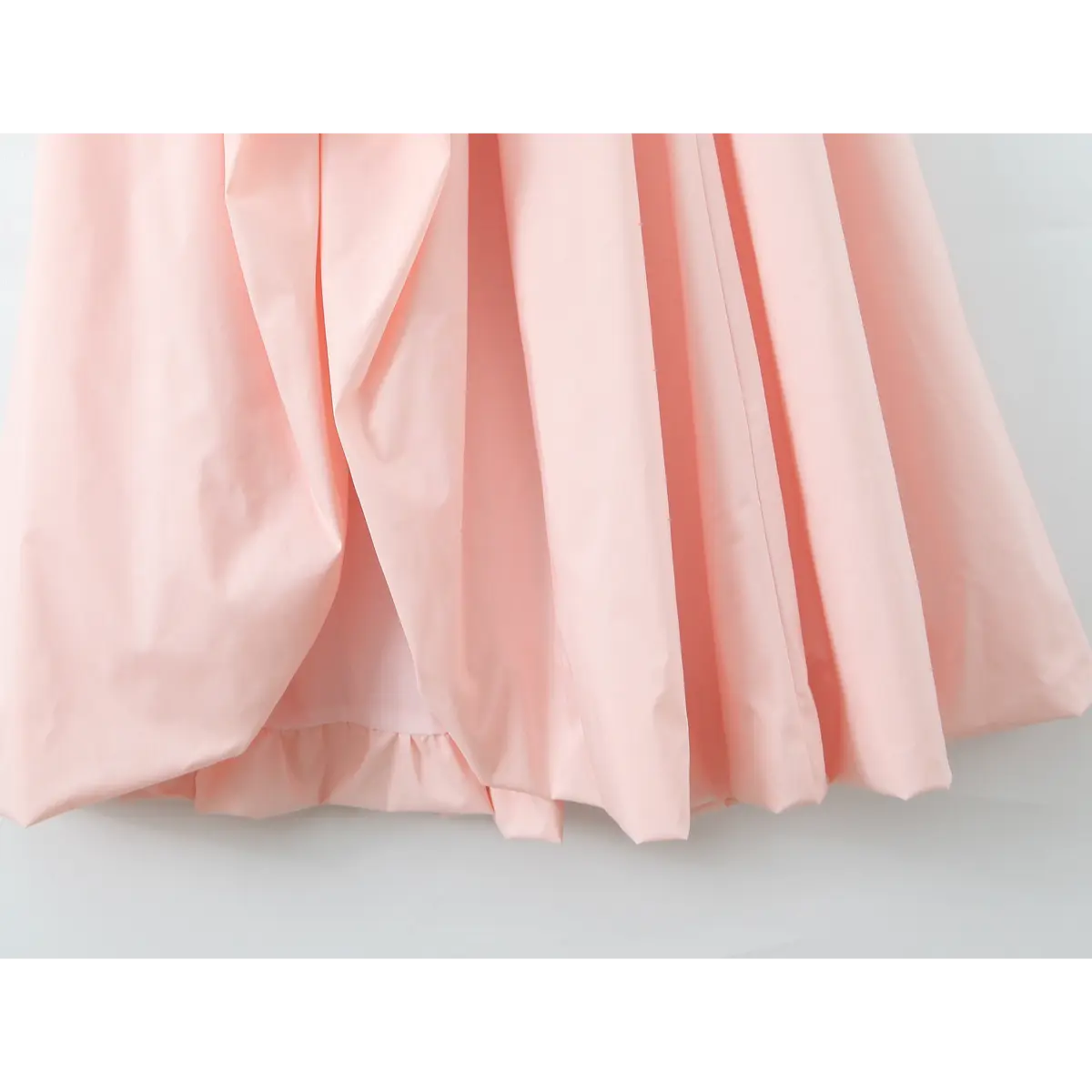 Close-up of the voluminous skirt hem of a light pink halter maxi dress, showing the gathered fabric and lining.
