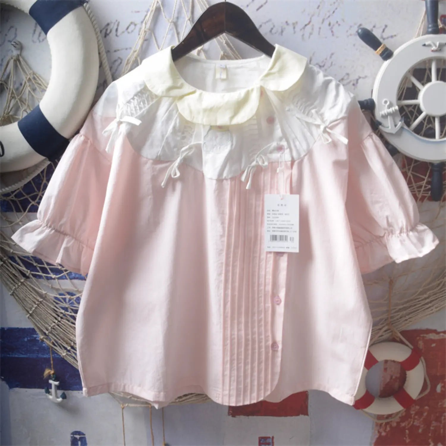 Light pink spliced peter pan collar bow short sleeve cotton blouse wooden hanger shot, cream ruffle doll collar shoulder white tiny bows front pleated tucks pink buttons puff ruffle cuff sleeves japanese sweet girl loose shirt hero shot