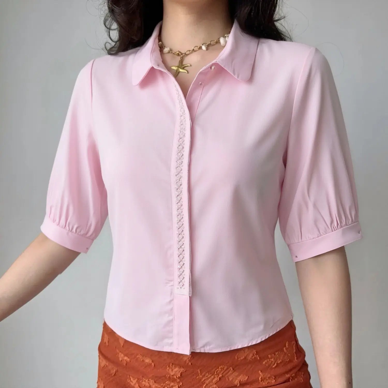 Female model wearing light pink collared cropped blouse with lace pearl front placket