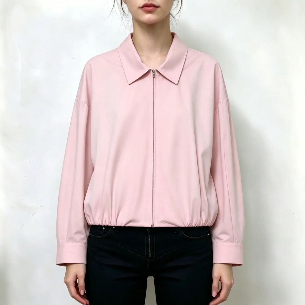 Model wearing light pink bomber jacket, classic point collar, full front zipper, long sleeves, elastic gathered hem, loose relaxed silhouette, paired with black jeans, plain white background